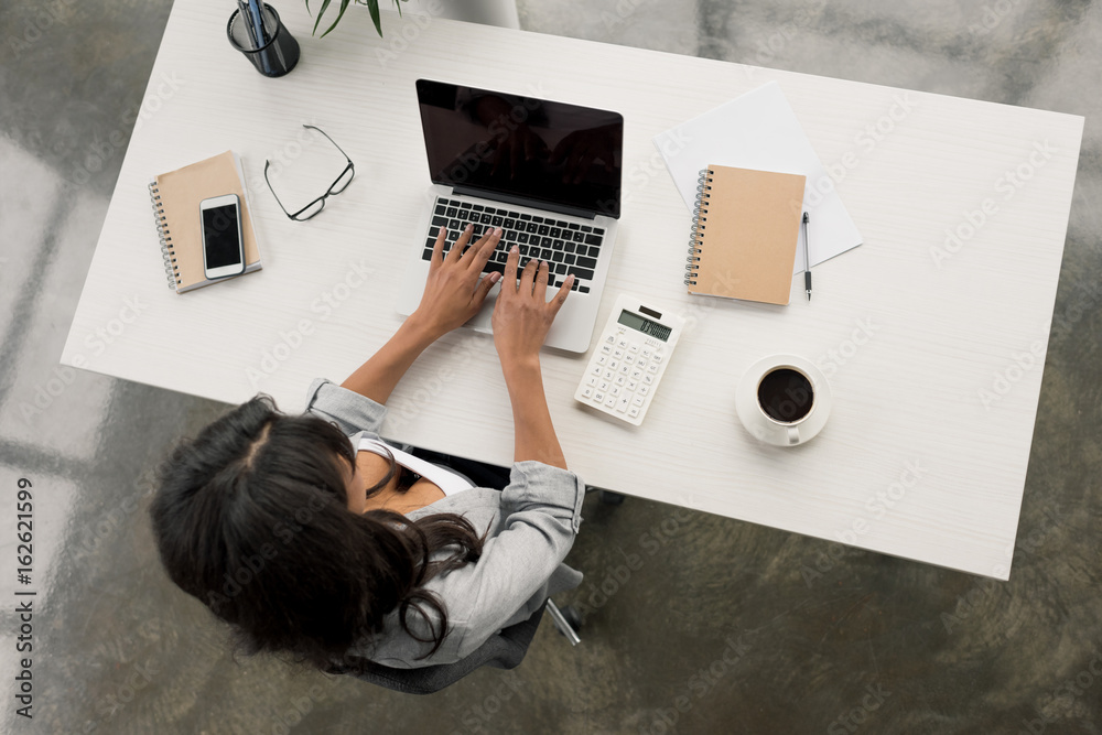 Φωτογραφία overhead view of businesswoman typing on laptop while sitting at workplace in of