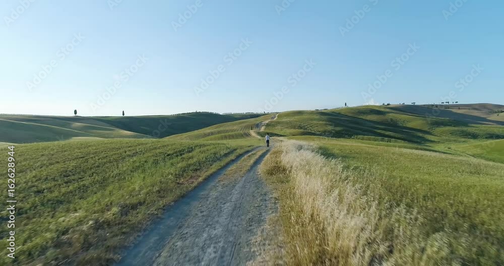 Forward aerial view of green wheat rural fields hills with road way. Nature outdoors travel destination Val d'Orcia, Tuscany, Italy. Daylight sunny summer or spring. 4k drone video shot Forward aerial view of green wheat rural fields hills with road way. Nature outdoors travel destination Val d'Orcia, Tuscany, Italy. Daylight sunny summer or spring. 4k drone video shot