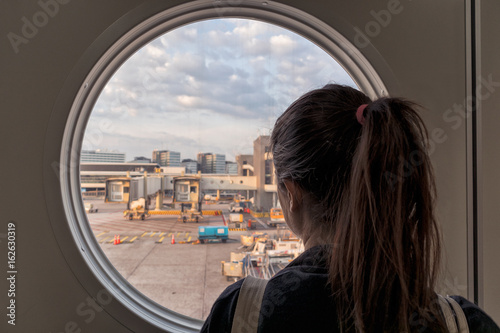 Wall Mural Girl looking through a round window at schiphol airport in amsterdam