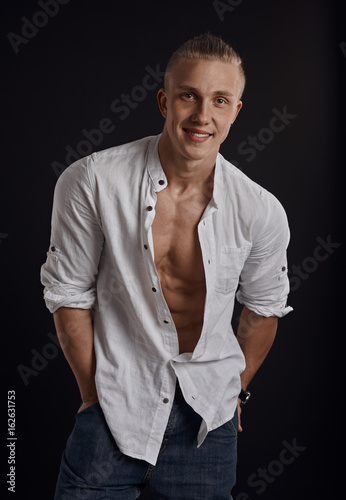 Handsome fit guy wearing unbuttoned white shirt posing in studio over black background.   © Stasique