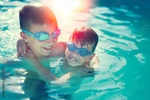 Happy little kids have fun in swimming pool graded in sunset