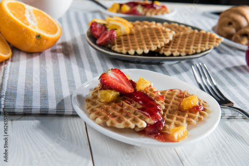 Close-up view of fresh homemade waffles with fruits and jam on table