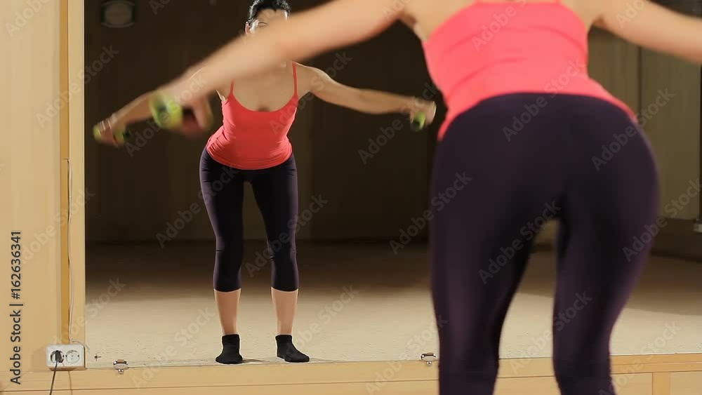Fitness woman engaged in the gym with dumbbell against the mirror. Perfect butt closeup. Athletic woman pumping up muscles with dumbbells. Fitness woman engaged in the gym with dumbbell against the mirror. Perfect butt closeup. Athletic woman pumping up muscles with dumbbells.