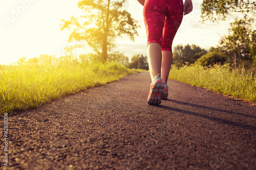 Sportliche Frau joggt einen Weg in der Natur bei Sonnenuntergang entlang - Konzept Sport, Fitness & Motivation 