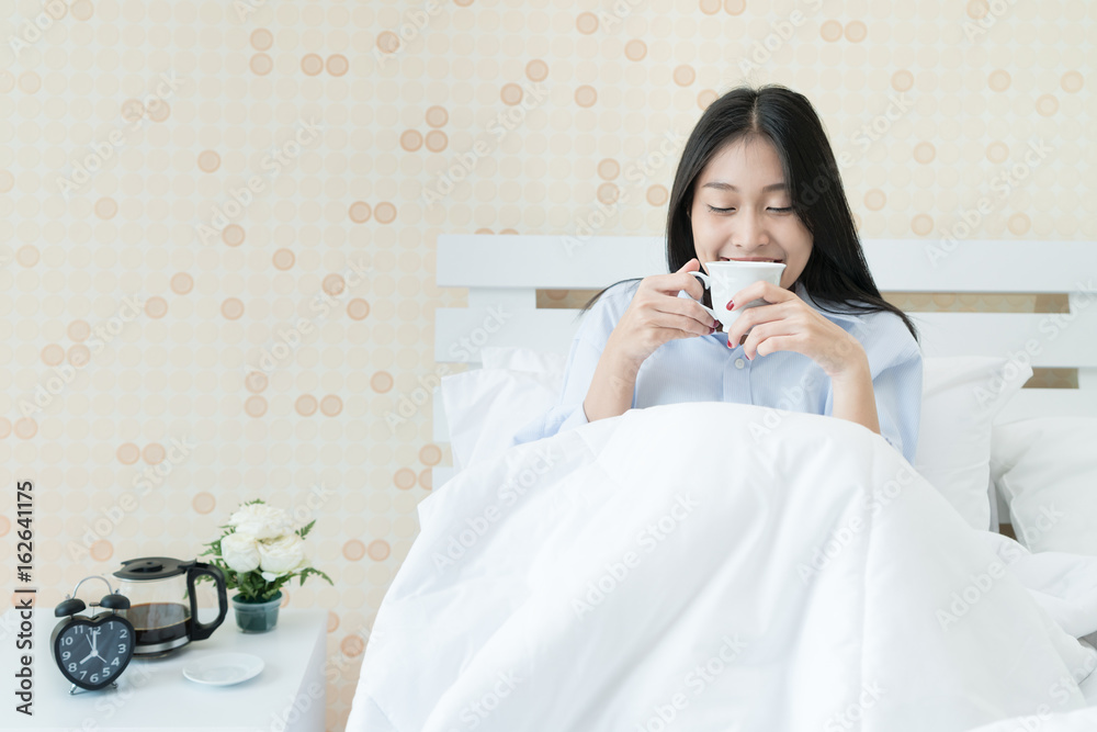 Asian young woman drinking coffee while sitting on bed in bedroom at home. Lazy sunny morning in bed. Asian young woman drinking coffee while sitting on bed in bedroom at home. Lazy sunny morning in bed.