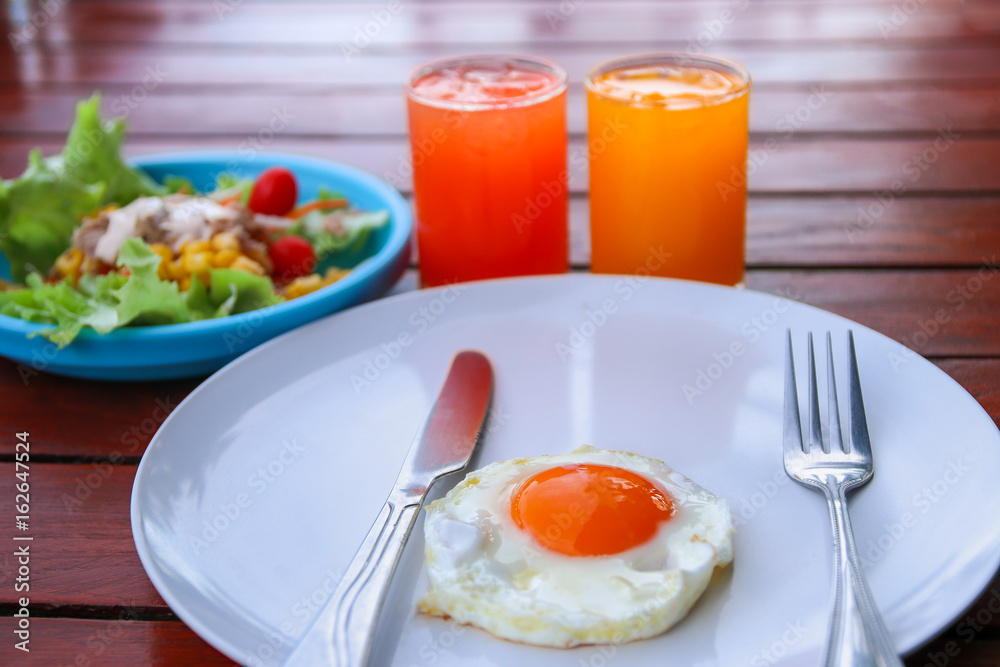 Healthy breakfast with fried egg, tuna salad and juice drink on wooden table.