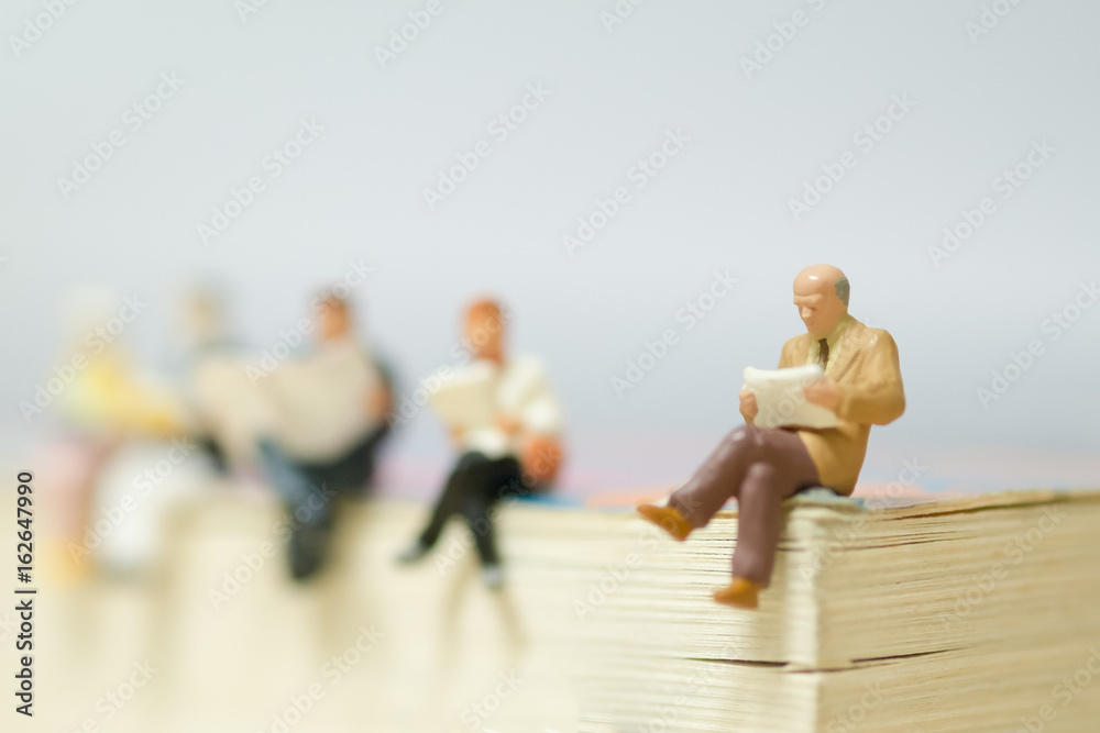 Miniature mini figures businessman sitting and reading on a big book,Improve knowledge and sharing. The benefits of reading concept