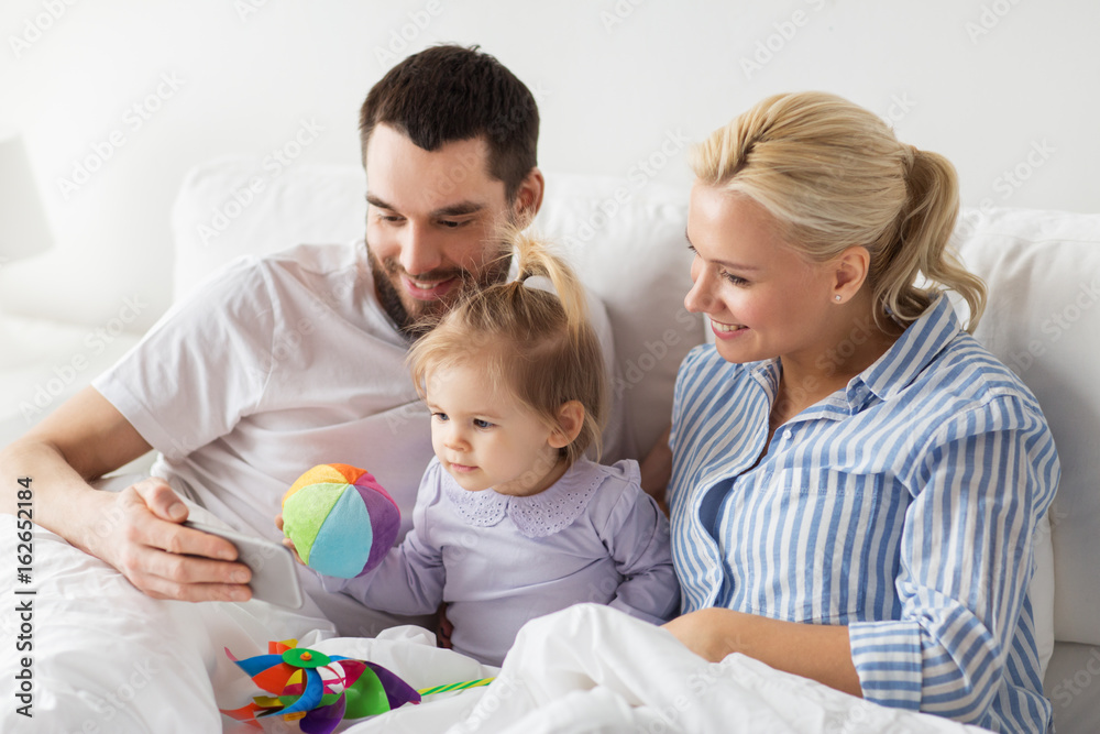 happy family with smartphone in bed at home happy family with smartphone in bed at home