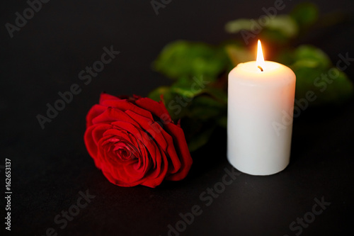 red rose and burning candle over black background
