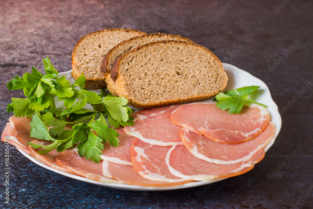 Fast snack. Smoked bacon, sliced thin slices, bread and fresh greens on a white porcelain dish on a dark background.
Fast snack. Smoked bacon, sliced thin slices, bread and fresh greens on a white porcelain dish on a dark background.
