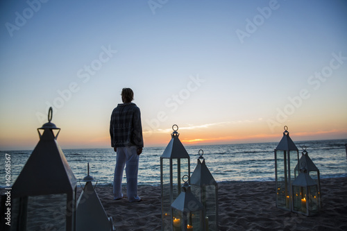 Rear view of man looking at sunset while sanding on beach