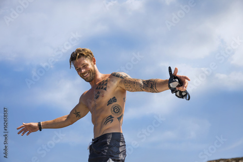 shirtless young man with tattoos on the beach
