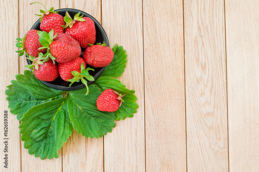 Fresh ripe strawberries in a plate on a wooden background. Top view.