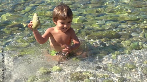 4K Two and a half years old boy plays with stones in pure sea water photo