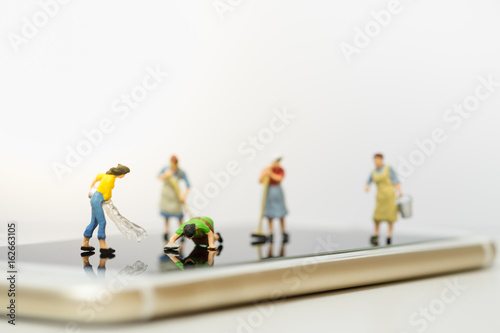 Technology concept. Group of women cleaner miniature figure washing and cleaning smart phone screen together.