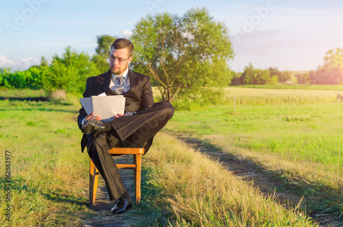 A man in a suit is studying documents sitting among nature, work on vacation. © mihakonceptcorn