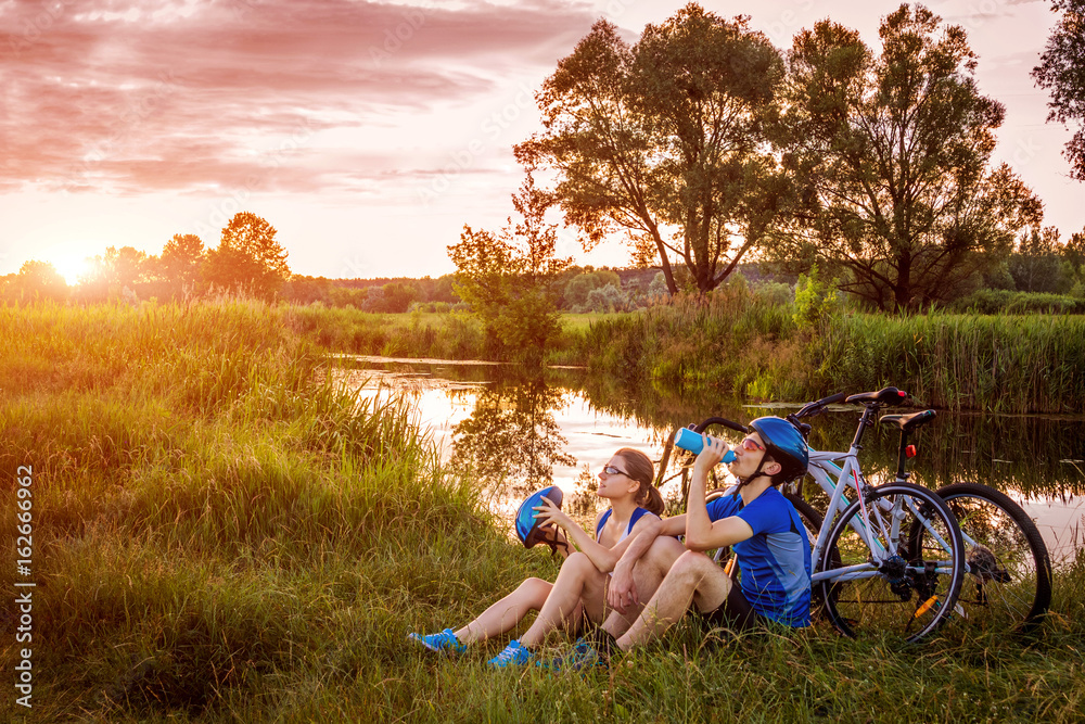 Fototapeta premium Couple of bicyclists having rest by the river