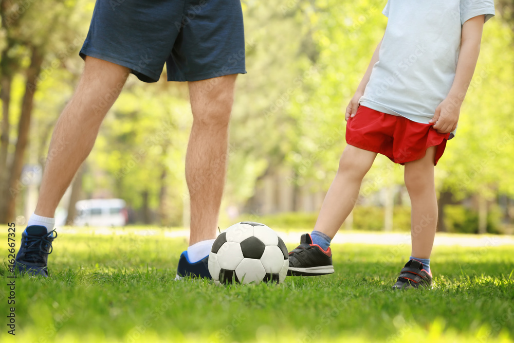 Father and son playing football on green grass in park Father and son playing football on green grass in park
