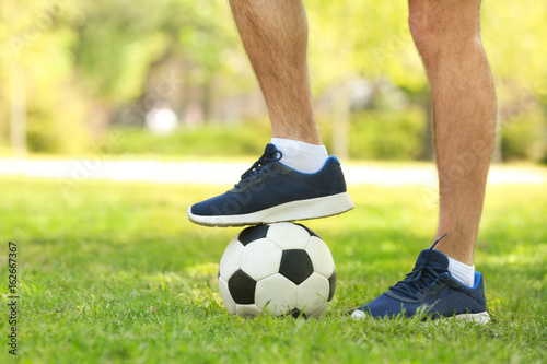 Legs of young man with soccer ball in green park on sunny day