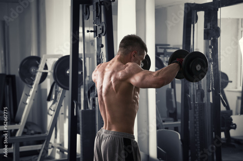 Bodybuilder workout with dumbbells in gym, perfect muscular male body