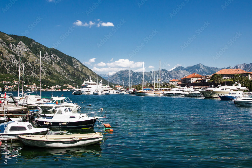 Kotor bay ships and boats in marina with beautiful mountain landscape in background.