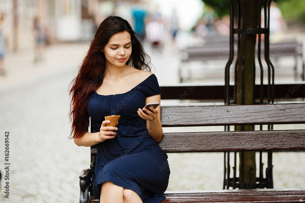 Teen girl using a smart phone and texting sitting in a bench. Beautiful  teens talk to smartphone and have fun in the city. Young beautiful smiling  woman talking on smartphone Photos