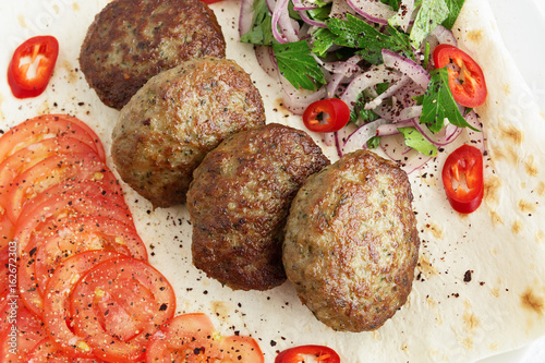kuru kofte on flat bread garnished with tomatoes, chili and salad of red onion and parsley