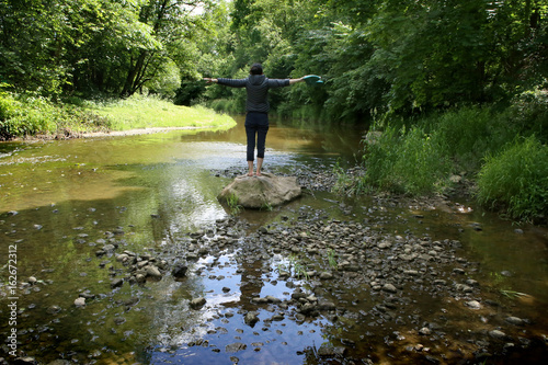 Woman in wild nature. Woman standing on stone in stream in summer.