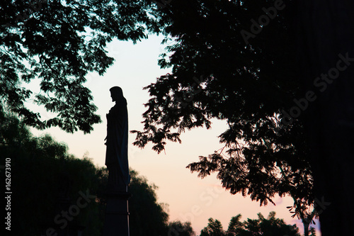 Silhouette of a statue from a cemetery at sunset seen from outside