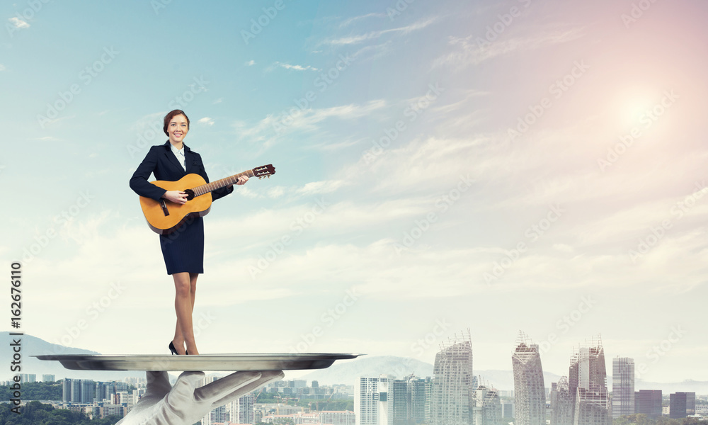 Attractive businesswoman on metal tray playing acoustic guitar against cityscape background Attractive businesswoman on metal tray playing acoustic guitar against cityscape background