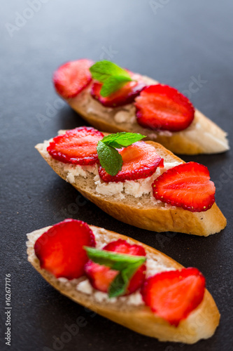 On a fashionable dark stone surface set sandwiches with cheese and strawberries, decorated with mint, tasty, healthy, breakfast, beautiful serve, berries, summer