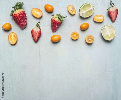 Fototapeta Naklejka Na Ścianę i Meble -  Healthy foods, cooking and vegetarian concept   sliced strawberries, lime and kumquat, space for text on wooden rustic background top view border