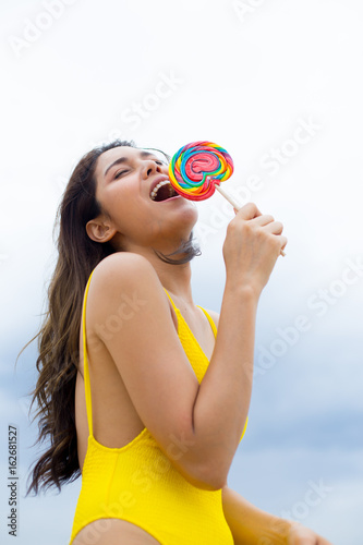 Happy young woman posing with lollipops at the beach in summertime