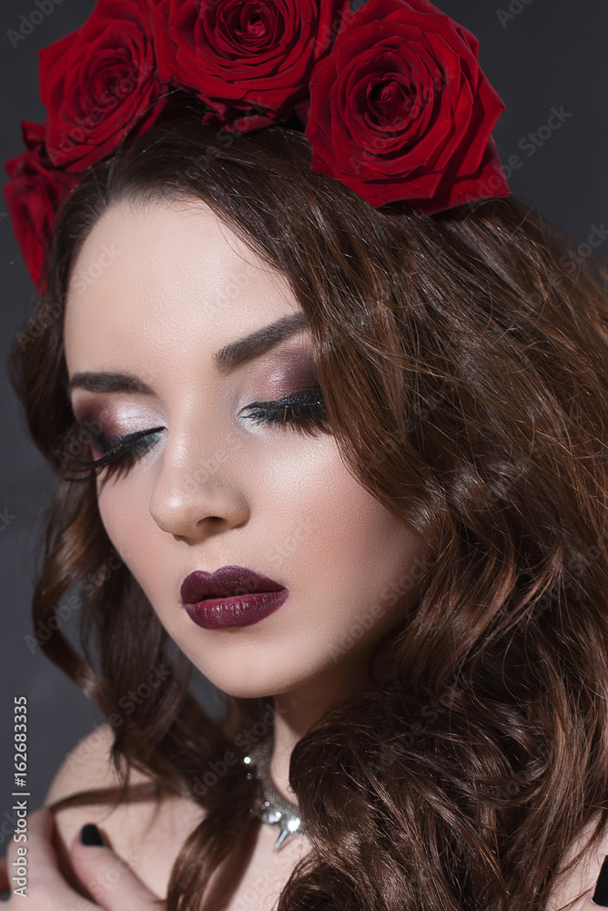 Fototapeta premium beautiful young woman with roses flower in hair. beauty girl with make-up over dark background. dark red lips.close-up fashion retouched portrait