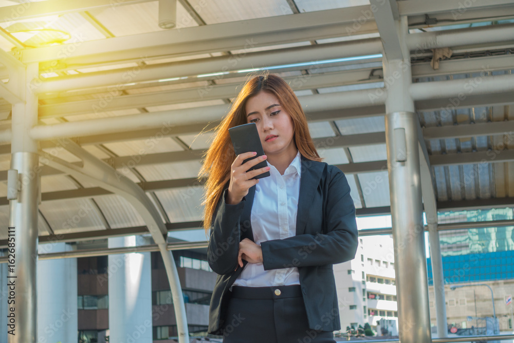 Beautiful Asian young businesswoman standing outside using a smartphone.