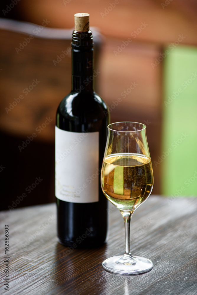 A glass with a white wine and the black wine bottle with label. Selective focus.