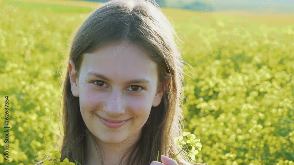 Smart young girl stands with rape flowers and smiling at camera in rape's field