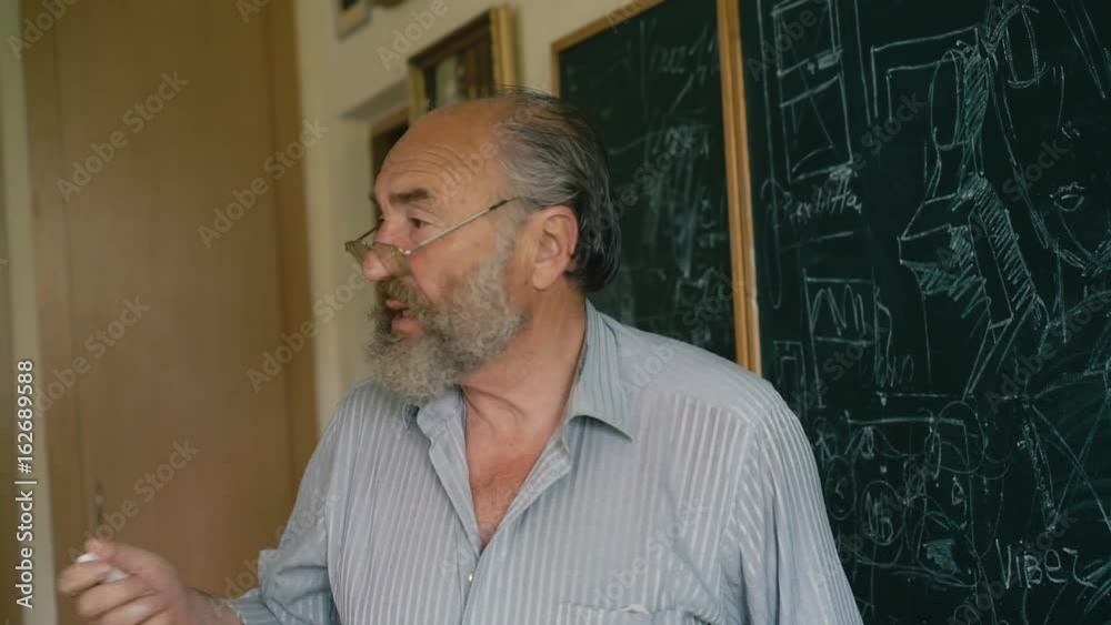 A charismatic old teacher explaining schemes near the blackboard 4K A charismatic old teacher explaining schemes near the blackboard 4K
