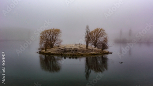 View of a small land in the middle of the lake during a foggy day in Twizel NZ