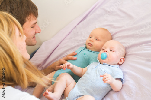 indoor portrait of young beautiful mother and father with baby, family with twins at home