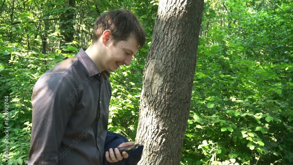 Young man stands in the woods, thinks about something and works on the phone. slow motion Young man stands in the woods, thinks about something and works on the phone. slow motion