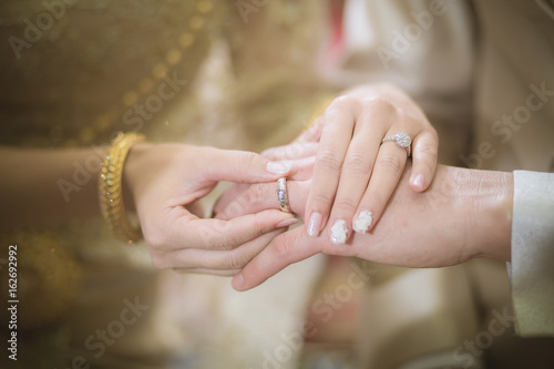 Thai groom wearing wedding ring for his bride
