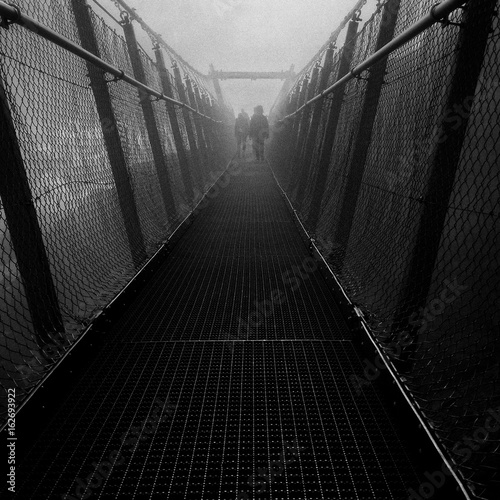 Obraz na plátně silhouettes walking on the bridge at Alps