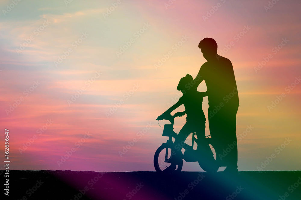 Fototapeta premium silhouette dad teach his daughter to bike on red sky background