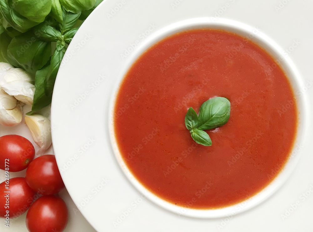 Vegetable tomato soup. Ingredients as tomatoes, garlic and basil herbs around the plate. Top view. Vegetable tomato soup. Ingredients as tomatoes, garlic and basil herbs around the plate. Top view.