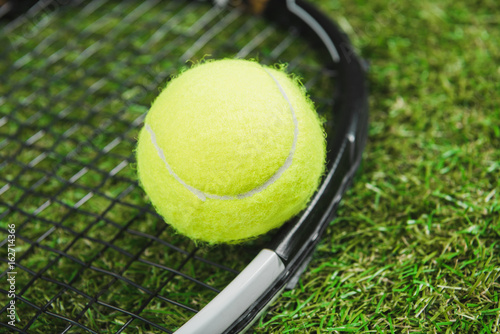 Close-up view of tennis racquet and ball on green grass