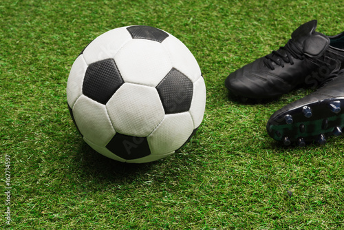 Close-up of soccer ball with pair of black sports shoes on grass