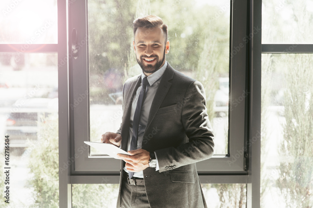 Fototapeta premium smiling businessman in suit using digital tablet at modern office