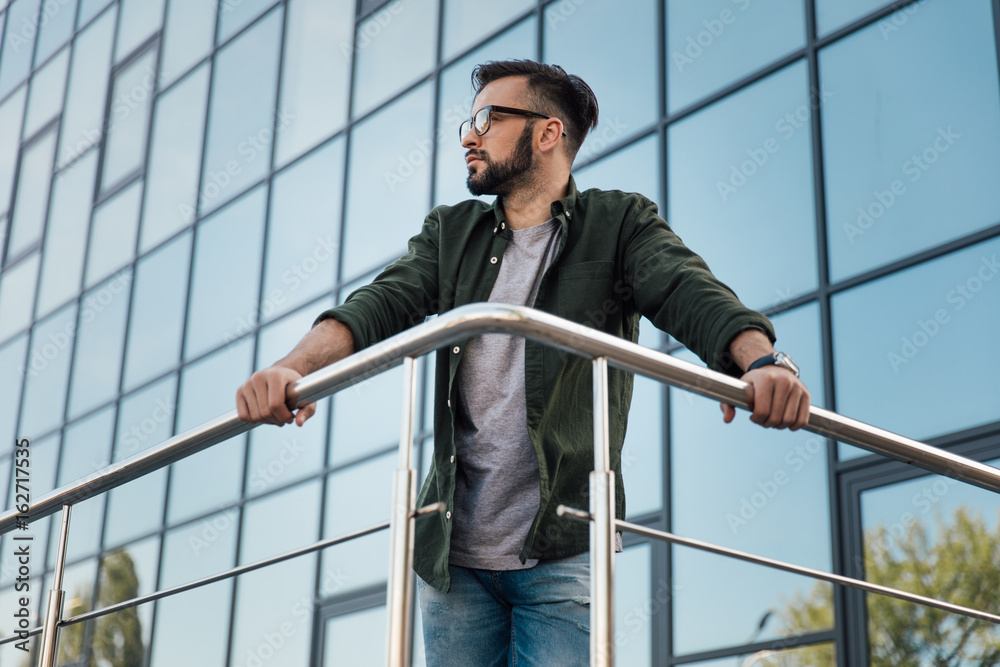 young bearded man in eyeglasses leaning on railing at office building young bearded man in eyeglasses leaning on railing at office building