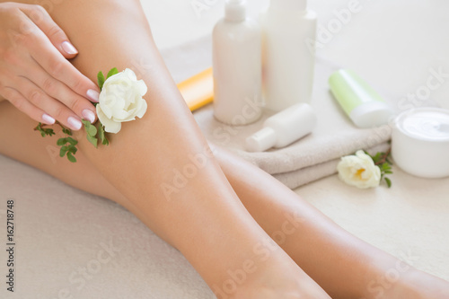 Woman's cares about a soft skin with body creams, lotions or oils in the bathroom after shower and shaving. Fresh white rose's gentle touch and scent.